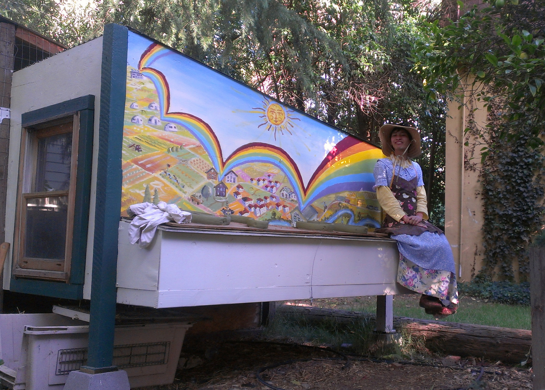 Alfred Twu sits on a chicken coop which Alfred and others collectively painted for WestCo, featuring each of the Davis Co-ops tied together by a rainbow.