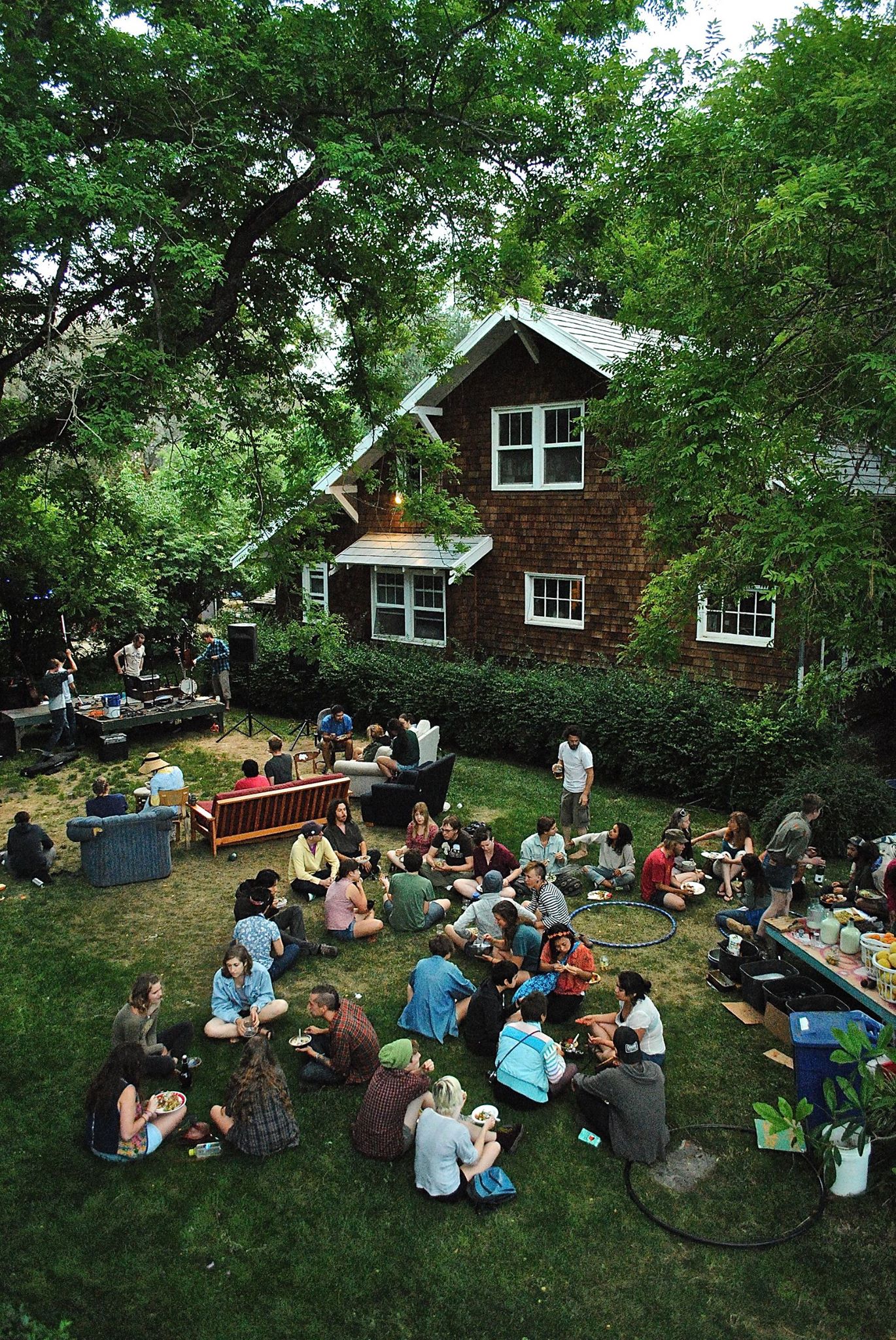 WestCo attendees share a meal outside, sitting on the grass, while watching a band prepare to perform.