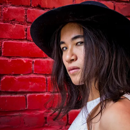 photo of Kai Cheng Thom against a red background wear a wide brimmed hat