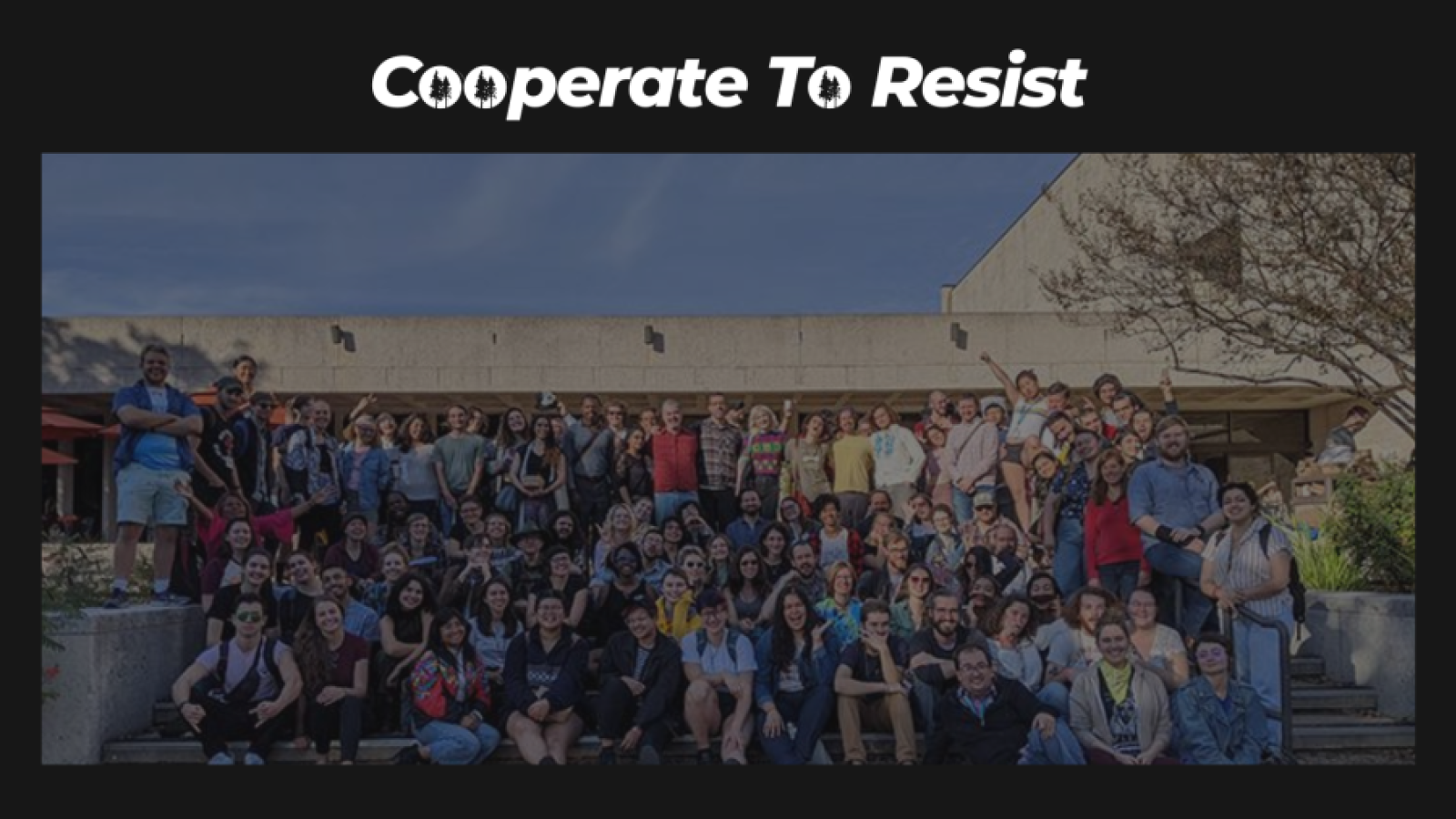 Text: Cooperate to Resist Fundraiser. Image: a large group of about 75 people posing for a group picture outside a building. Happy excited postures for cooperatives!